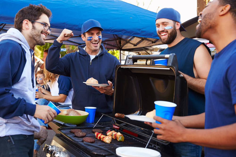 A group of men hang out around a grill at a college football tailgate, one of the best sporting events for RVing
