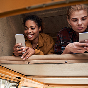 Two girls searching old RV owner's manuals in their Class B motorhome on smartphones