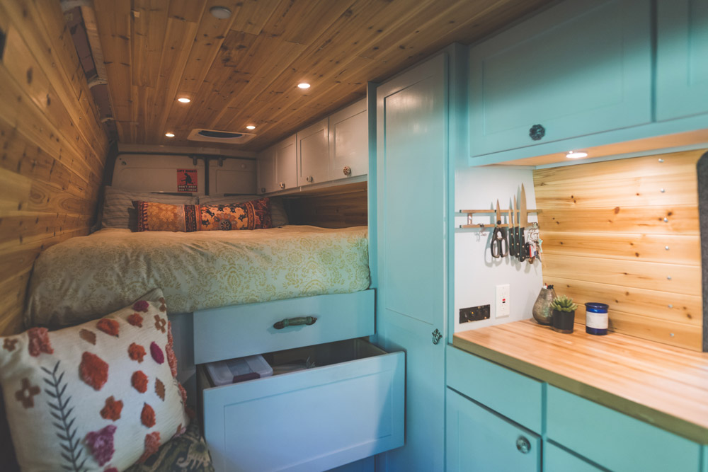 The interior of a camper van with blue cabinets and a tidy bed. Your RV can look this clean with our camper storage ideas