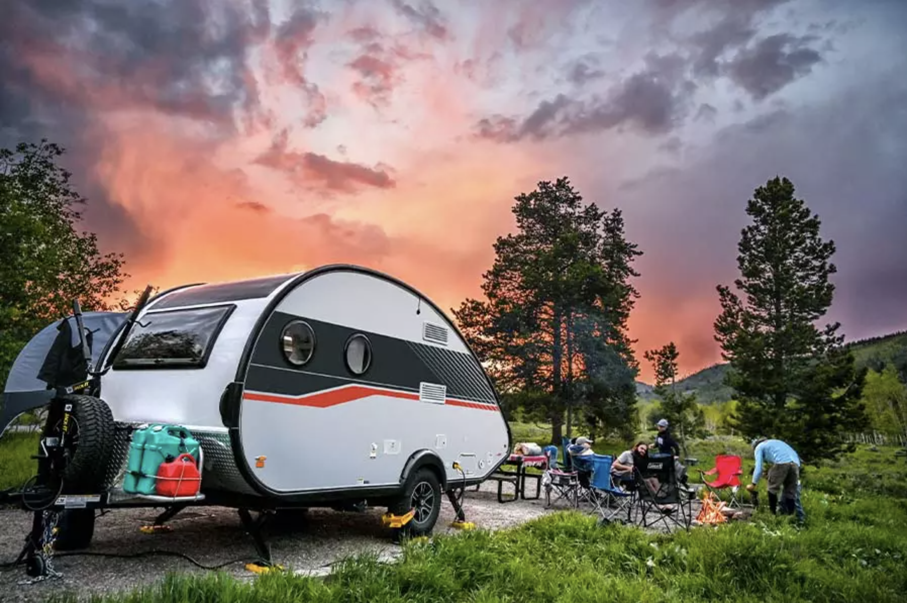 The Nucamp TAB 400 is one of the coolest small campers. This picture shows the teardrop trailer parked at a campsite in front of a vivid sunset.