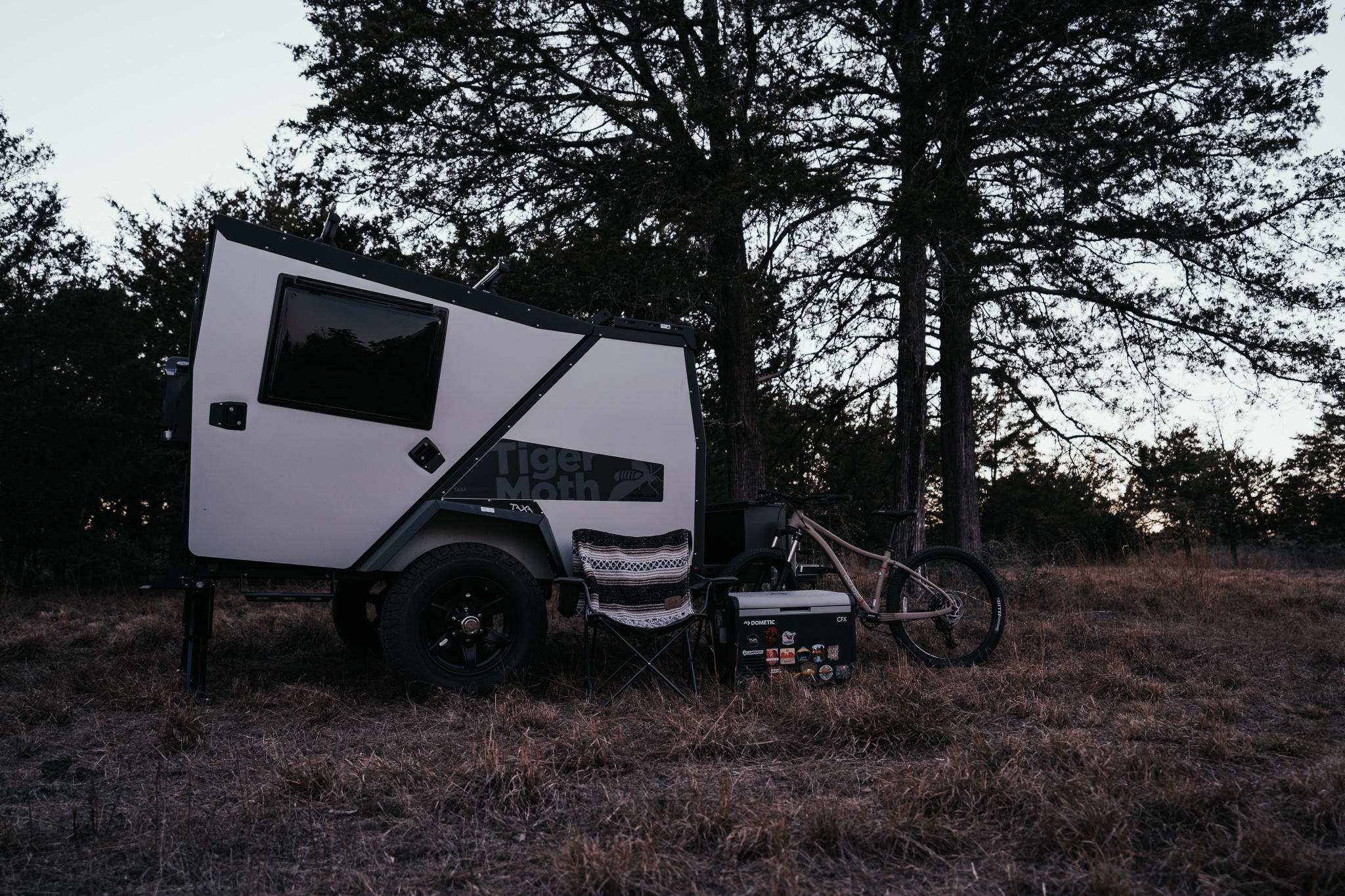 A TAXA TigerMoth Overland camps in the forest at dusk. This is one of the coolest small campers on the market.