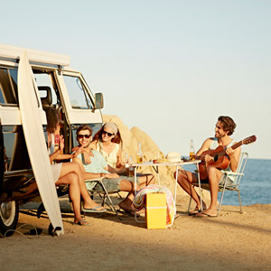 A group of friends sit outside a camper van by the beach on their summer RV travels