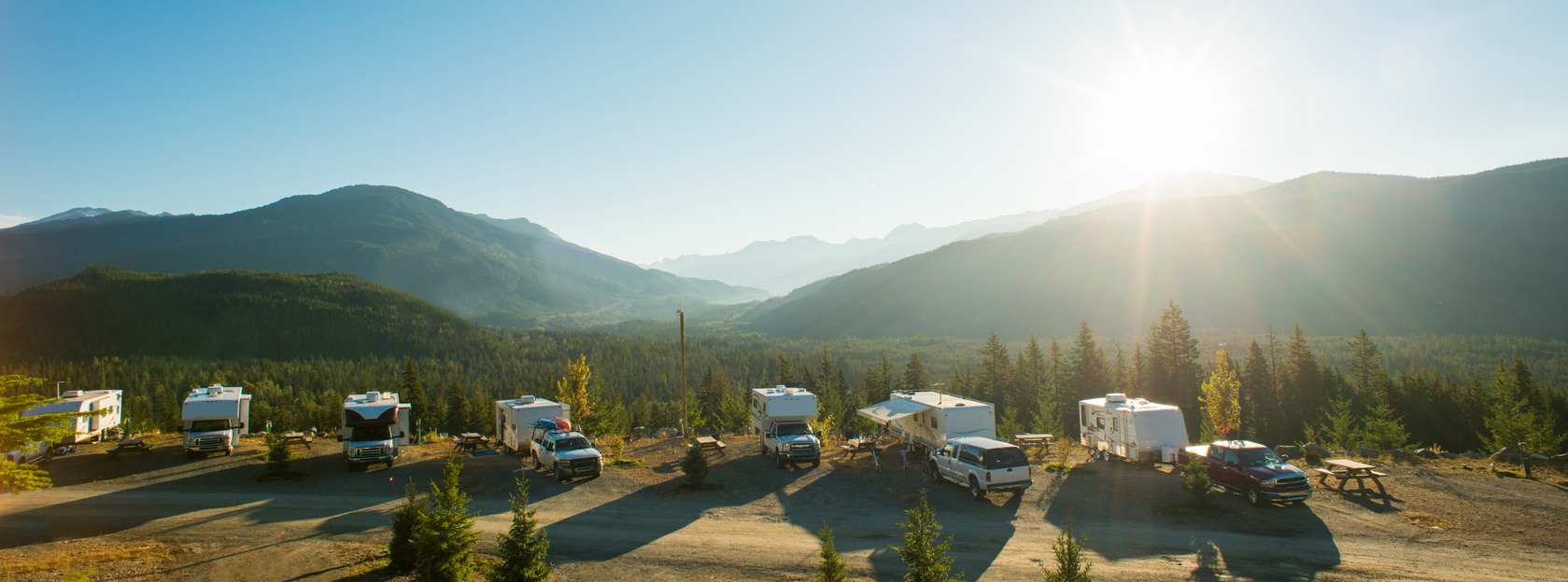 RVs parked at a campsite in the mountains as the sun shines overhead