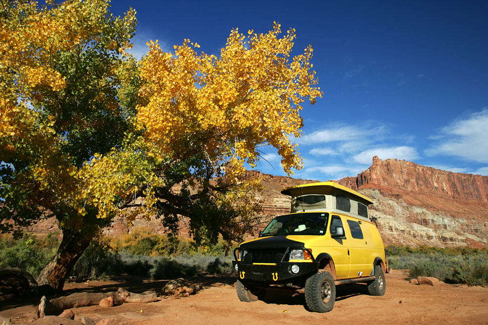 Overland camper van sits among fall trees in a Utah landscape