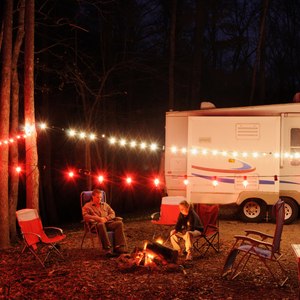 Rv christmas decorations on a camper with lights and a couple sitting outside at a fire