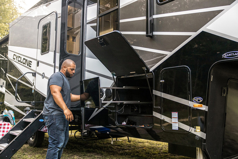 A man sets up his outdoor entertainment center on his Heartland Cyclone, one of the best RVs for 2022