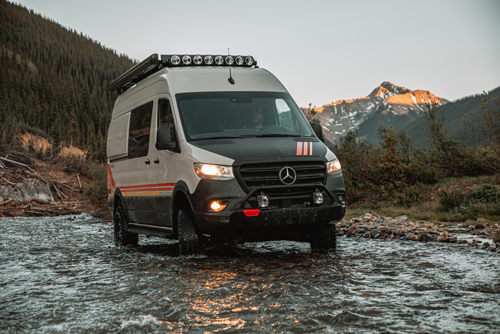 A Storyteller Overland van drives through water in the mountains. This is one of the overland RVs for sale on RVUSA