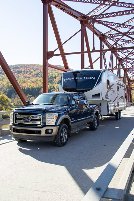 A truck drives a Grand Design Reflection over a bridge with fall foliage. This is one of the top 10 most viewed RVs on RVUSA