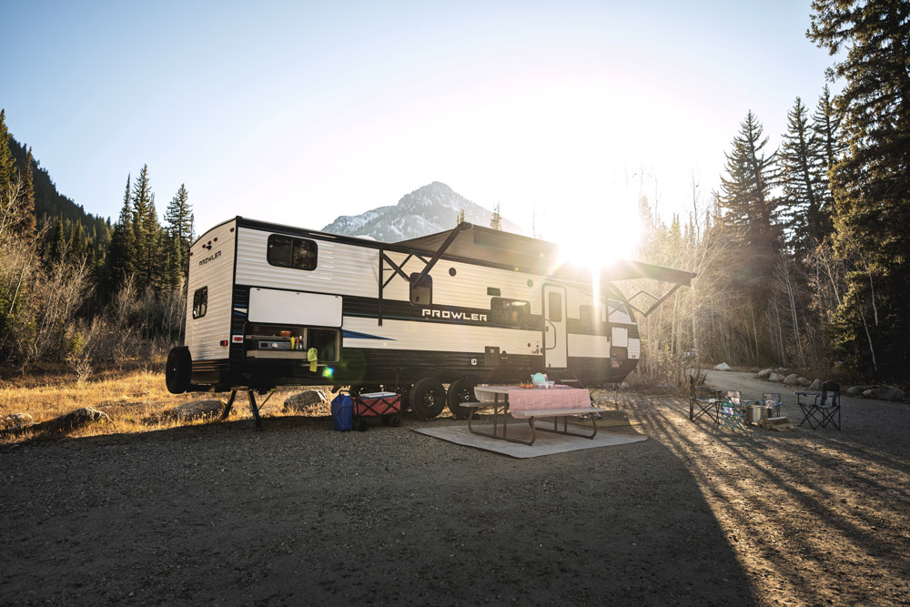 A Heartland Prowler RV parked with a mountain and sun rays in the background