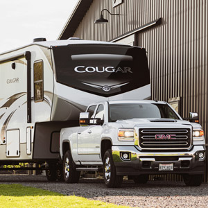 A Keystone Cougar fifth wheel is hitched up to a truck in front of a horse barn