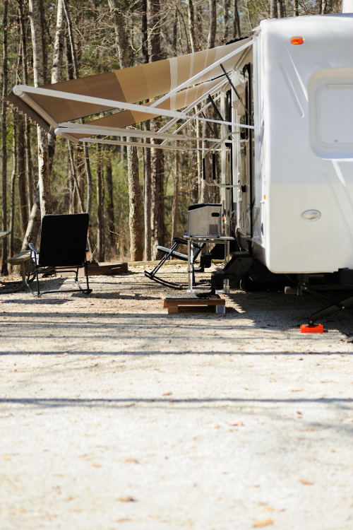 An RV sits parked at a campsite with its RV awning unfurled