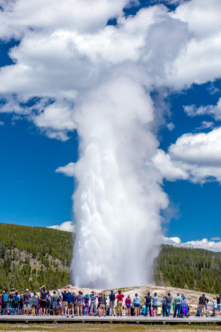 Visitors crowd around the viewing area as Old Faithful geyser erupts