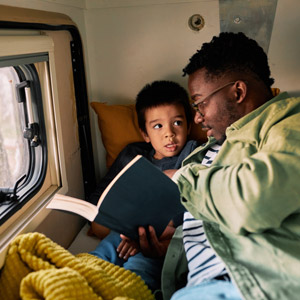 A dad reads to his son in an RV. Treat your RVing dad with a gift from one of these RV gifts for dad