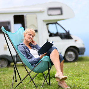 A woman reads a book outside her RV. Our recommendations for camping and RVing books will help make you a better RVer.