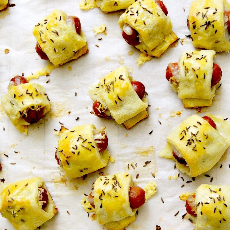 Pigs in a blanket scattered around parchment paper. If you're looking for RV tailgating recipes, you need this!