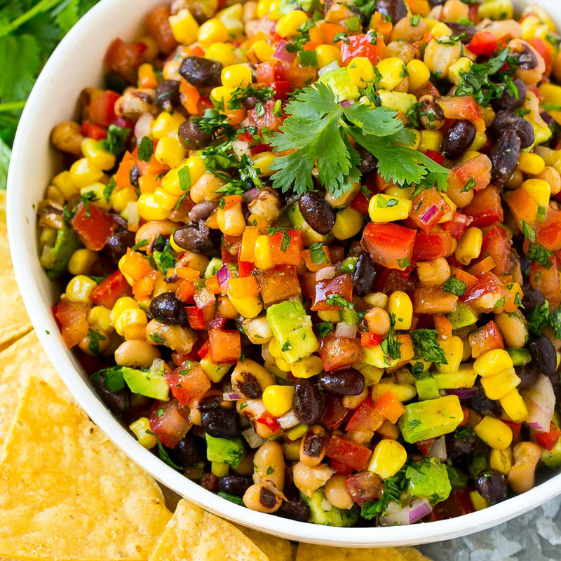 A bowl of cowboy caviar with chips beside it.