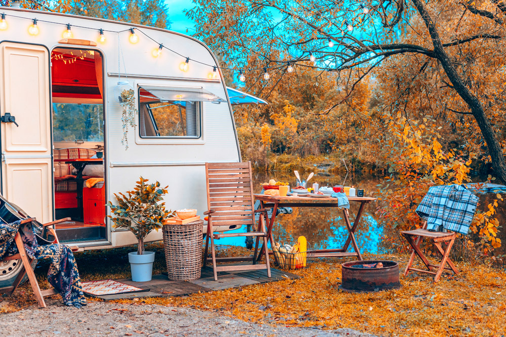 A camper with fall RV decor sits beside a lake with fall color around it.