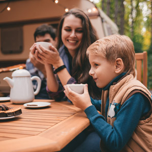 A boy holds a mug of tea while camping with his family during fall. Adding fall RV decor to your camper can make cozy nights like this even better