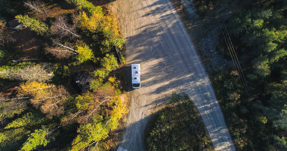An aerial view of an RV boondocking on a dirt road surrounded by trees. Making more eco-friendly RVs is a growing trend that came from the 2022 Hershey RV Show.