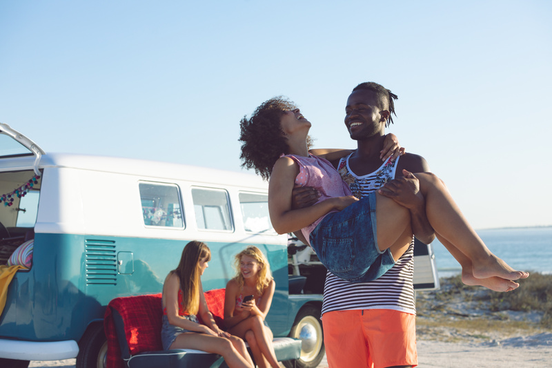 A group of young people outside of a vintage RV on the beach, where RV mold prevention is important.