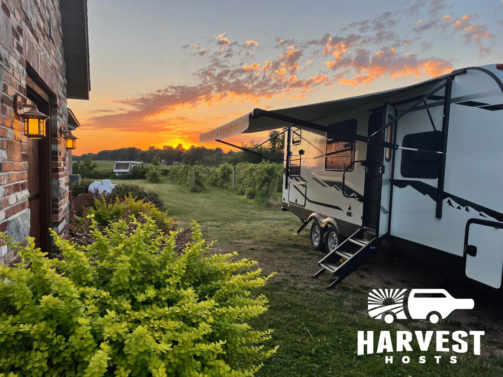 An RV sits on a farm with a beautiful sunset in the background as part of a Harvest Hosts stay.